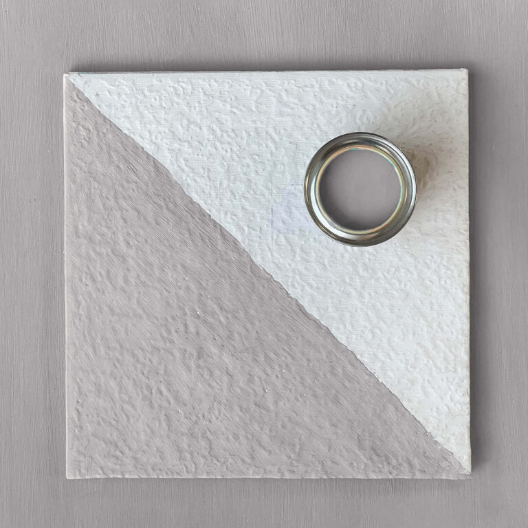 Textured white and gray square tile with a circular metallic object on a gray background