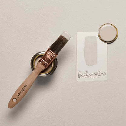 Paintbrush and paint can with color swatch labeled 'feather pillow' on a neutral background