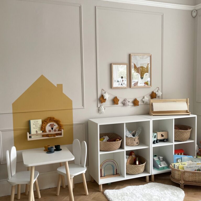 Children's playroom with white storage unit, table, and chairs against a light gray wall.