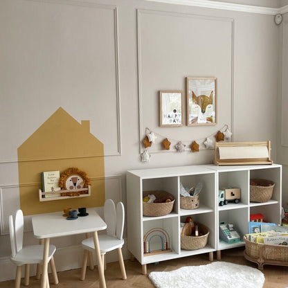 Children's playroom with white storage unit, table, and chairs against a light gray wall.