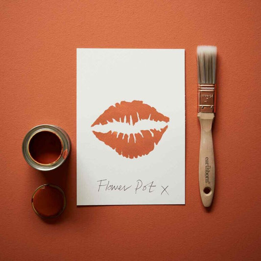 Paint can, brush, and paper with a lipstick print on an orange background