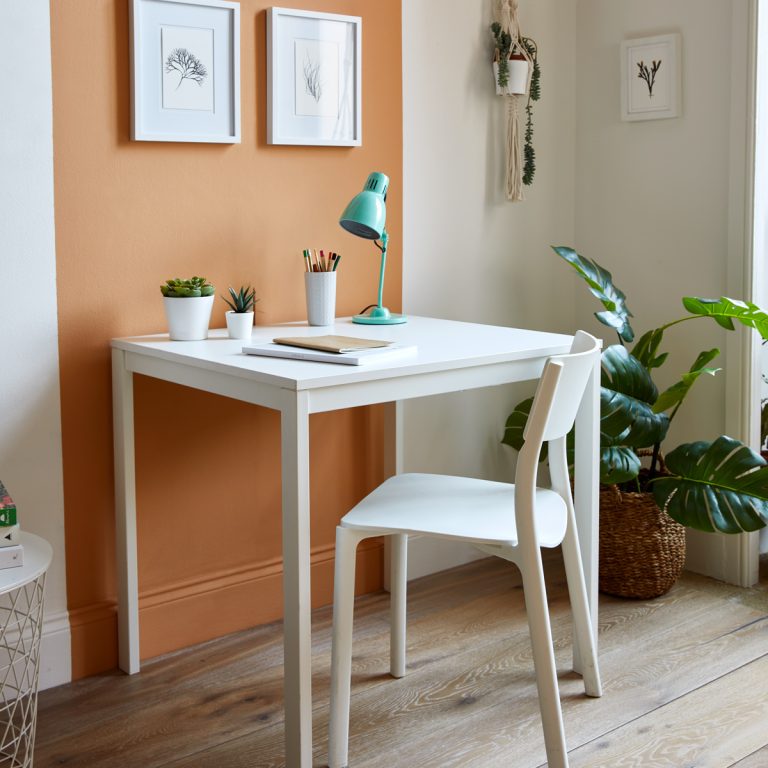 White desk with a chair in a room with an orange wall and plants.