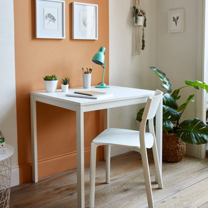 White desk with a chair in a room with an orange wall and plants.