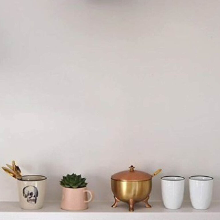 Collection of decorative items including mugs, a pot, and a brass container on a white surface with a light gray background.