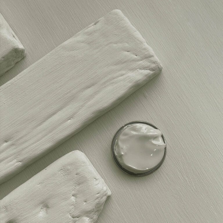 Close-up of white paint swatches and a small container on a light gray surface