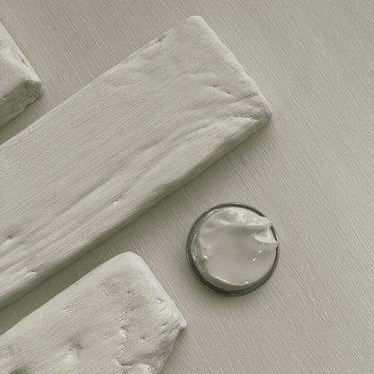 Close-up of white paint swatches and a small container on a light gray surface