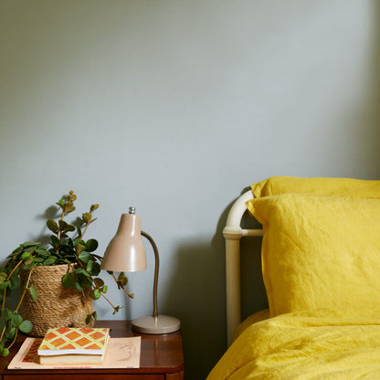 Yellow bedspread on a bed with a lamp and plant on a nightstand against a light blue wall.