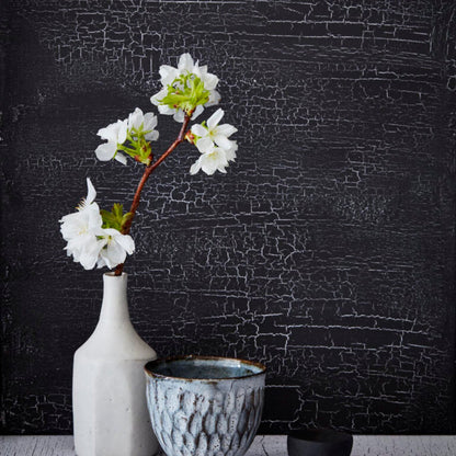 White vase with flowers against a textured black wall