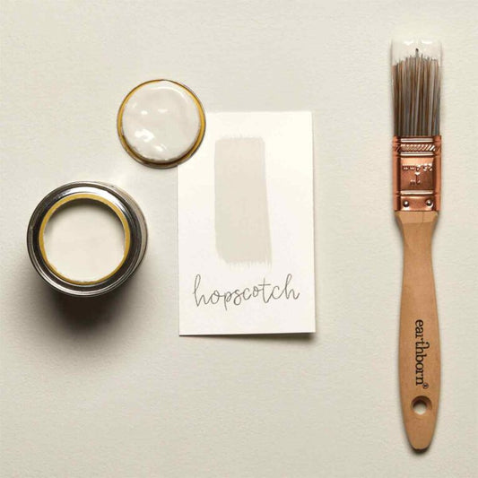 Two paint cans, a paintbrush, and a piece of paper with 'hopscotch' text on a light gray background.