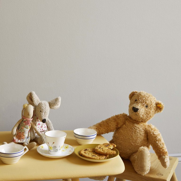 Stuffed animals, including a bear and a rabbit, sitting at a table with tea cups and cookies.