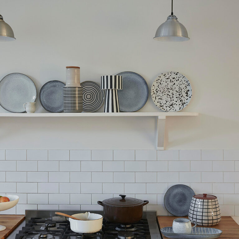 Kitchen with shelves displaying ceramic plates and bowls, and a stove with pots and pans.