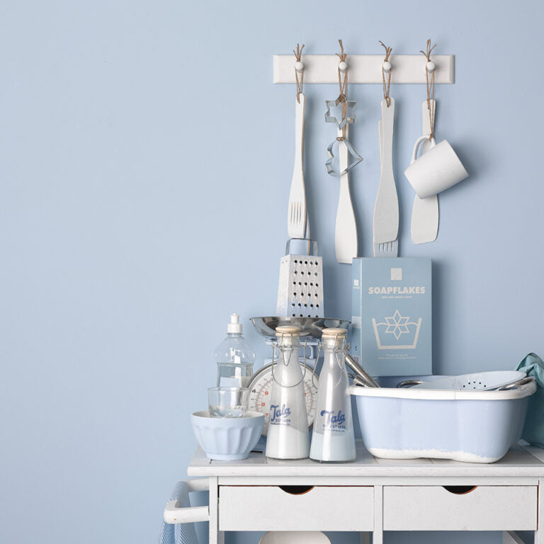 White wall-mounted hook with kitchen utensils and containers against a light blue wall.