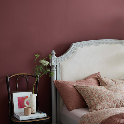 Bedroom with a bed featuring pillows and a side table with decor items against a maroon wall.