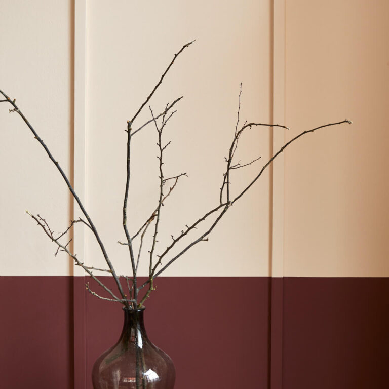 Glass vase with bare branches against a two-tone wall.