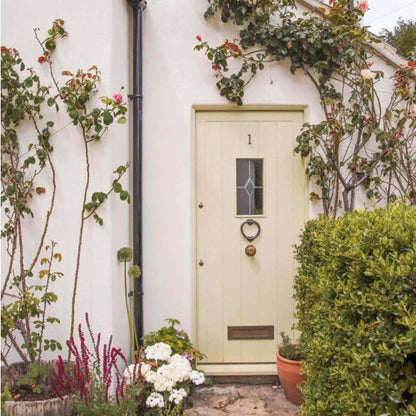 Cottage door with decorative heart-shaped handle, surrounded by plants and flowers.