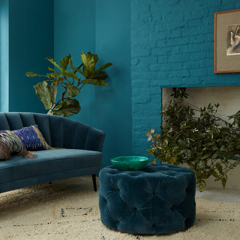 Blue living room with a tufted ottoman, sofa, and plants.