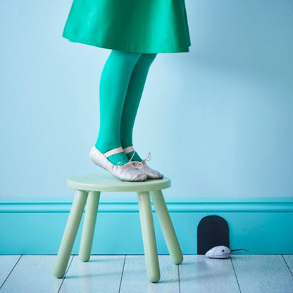 Person wearing a green skirt and leggings standing on a small stool against a light blue wall.