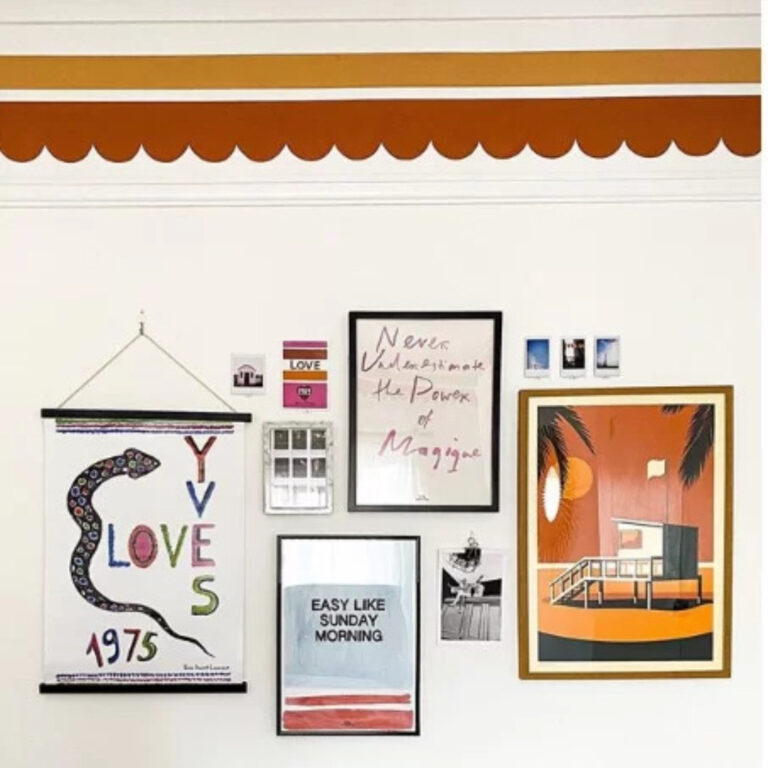 Wall with various framed posters and art pieces on a white wall.