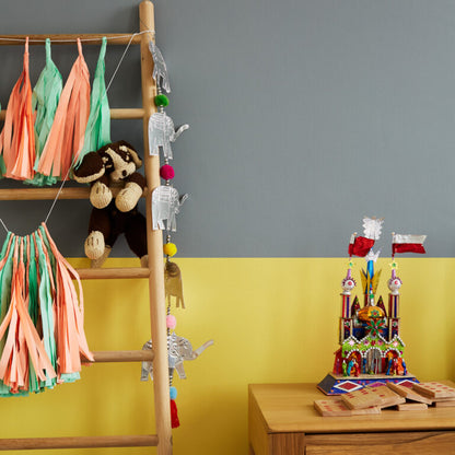 Children's room with a ladder, colorful tassels, and toys against a gray and yellow wall.