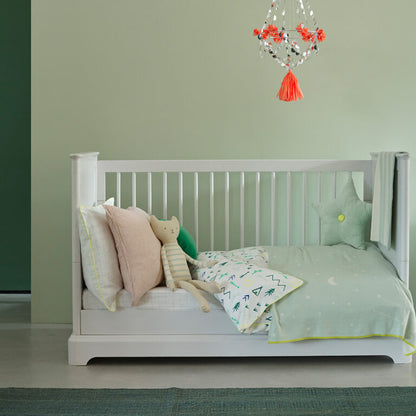 White crib with bedding and a teddy bear in a room with a green wall and decorative hanging light.