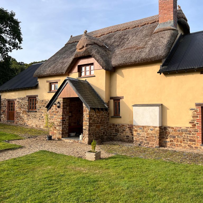 Thatched roof house with stone foundation and green grass in front