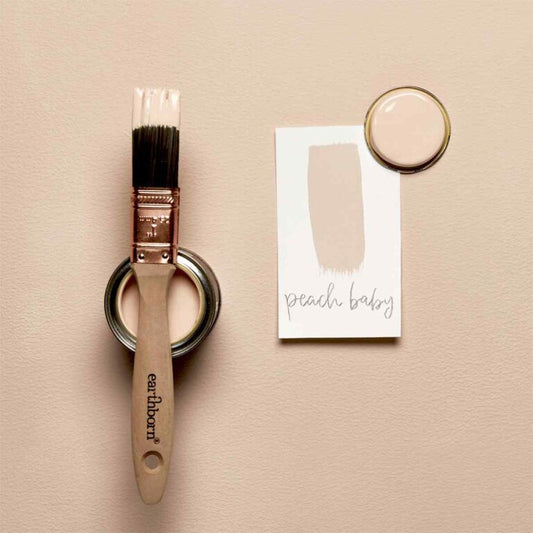 Paintbrush and paint sample with 'peach baby' color swatch on a beige background
