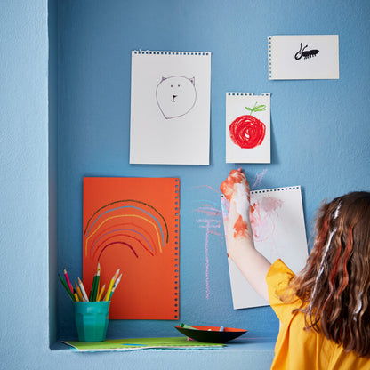 Child drawing on a whiteboard with colorful pencils and art supplies on a blue wall.