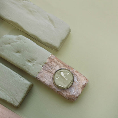 Jar of cream on a rock with two large blocks of cream beside it on a light green background
