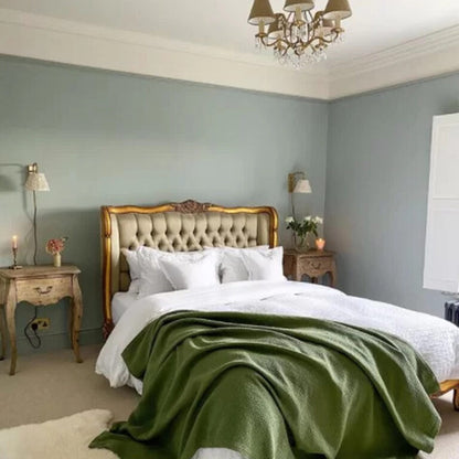 Neatly made bed with a green throw blanket in a bedroom setting.