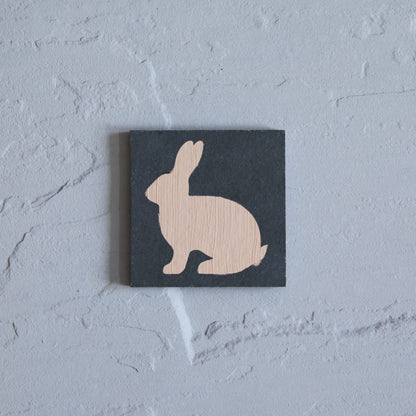 Wooden rabbit silhouette on a black square background against a light gray wall
