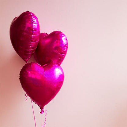 Three pink heart-shaped balloons against a light pink background