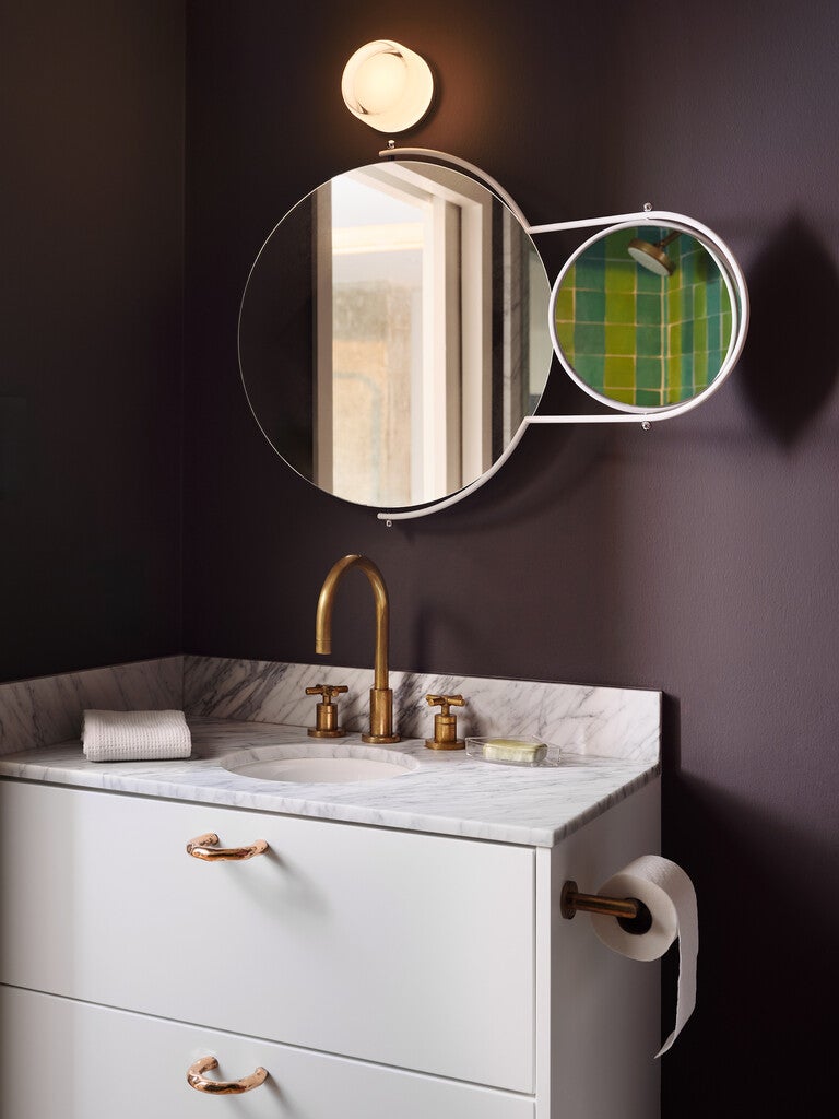 Bathroom vanity with round mirror and marble countertop against a dark wall.