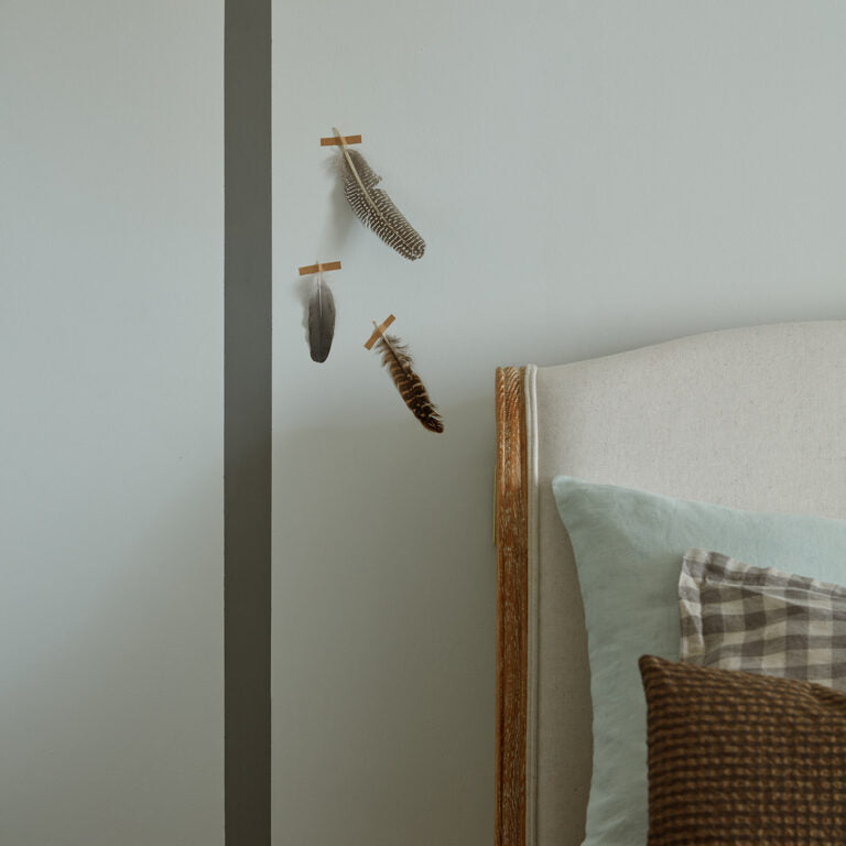 Decorative feathers on a wall next to a bed with pillows