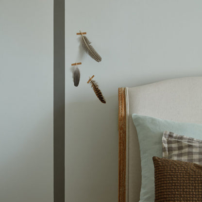 Decorative feathers on a wall next to a bed with pillows