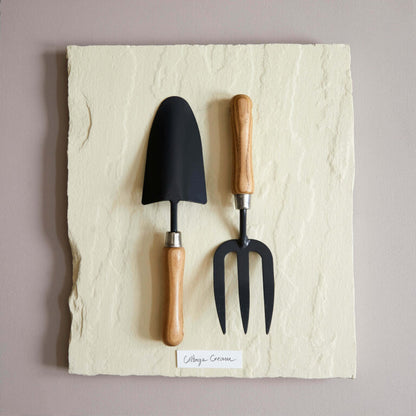 Gardening tools with black heads and wooden handles on a textured stone surface.