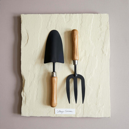 Gardening tools with black heads and wooden handles on a textured stone surface.