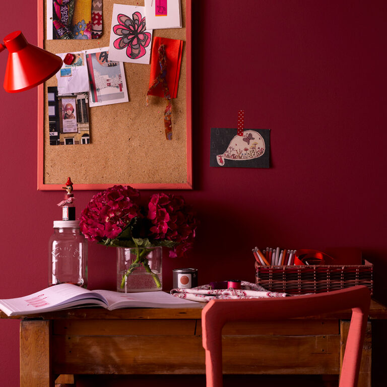 Home office with a red wall, cork bulletin board, desk, and chair.