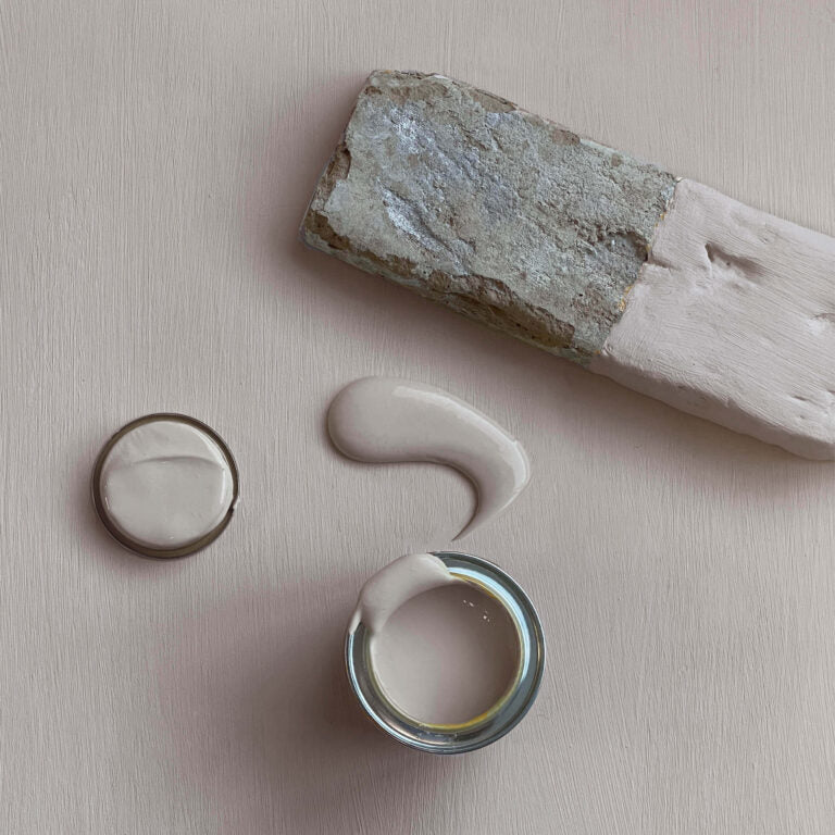 Paint can with lid, stone, and paint swatch on a beige background