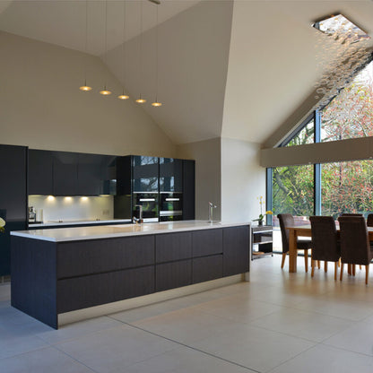 Modern kitchen with black cabinetry and white countertops, featuring a dining area in the background.