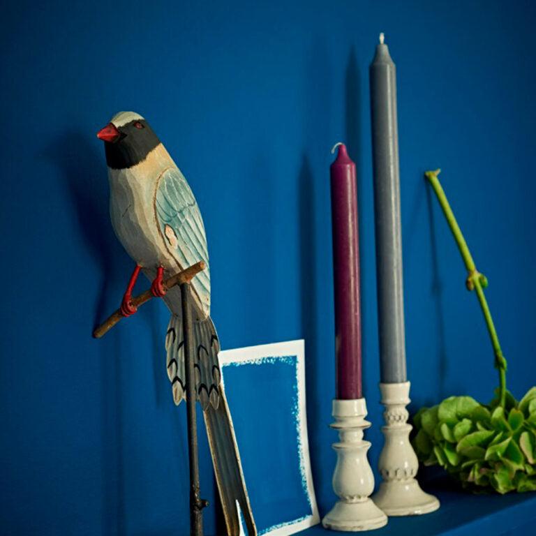 Decorative bird figurine, candles, and plant against a blue background