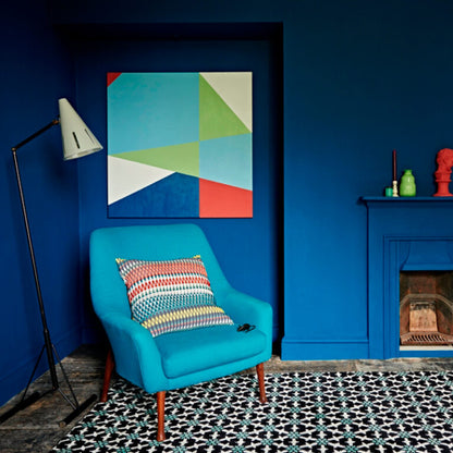 Blue armchair with a colorful pillow in a room with blue walls, a fireplace, and abstract art.
