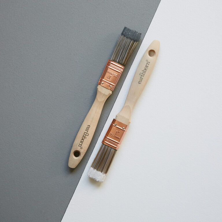 Two paint brushes with wooden handles and copper ferrules on a gray and white background.