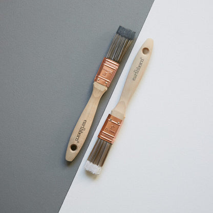 Two paint brushes with wooden handles and copper ferrules on a gray and white background.