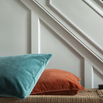 Two pillows, one teal and one orange, on a textured surface with a white paneled wall in the background.