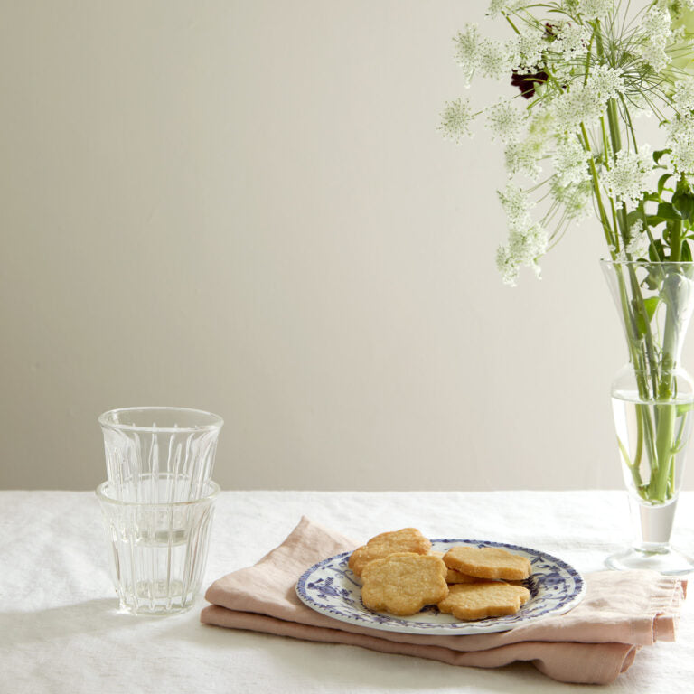 Table setting with cookies, glasses, and a vase of flowers on a neutral background