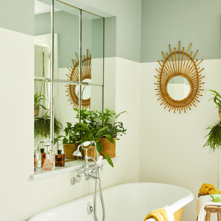 Bathroom with a sunburst mirror, bathtub, and plants