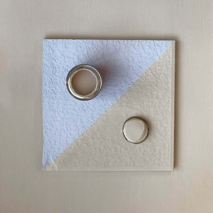 Two rings on a textured square card with a light blue and beige design.