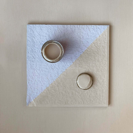 Two rings on a textured square card with a light blue and beige design.