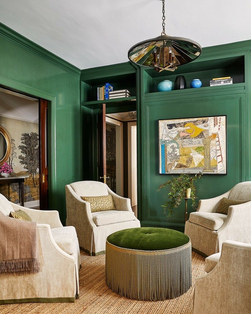Luxurious living room with green walls, white chairs, and a green ottoman.