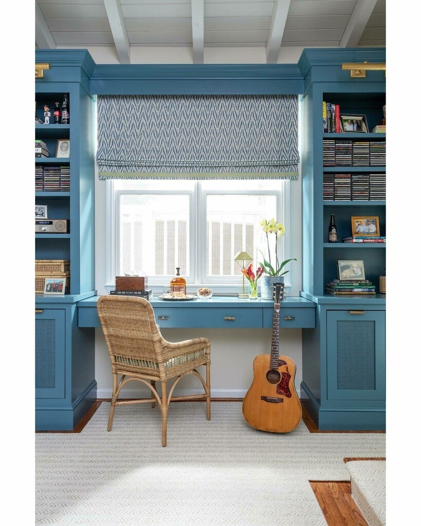 Home office with blue bookshelves, a desk, guitar, and chair.